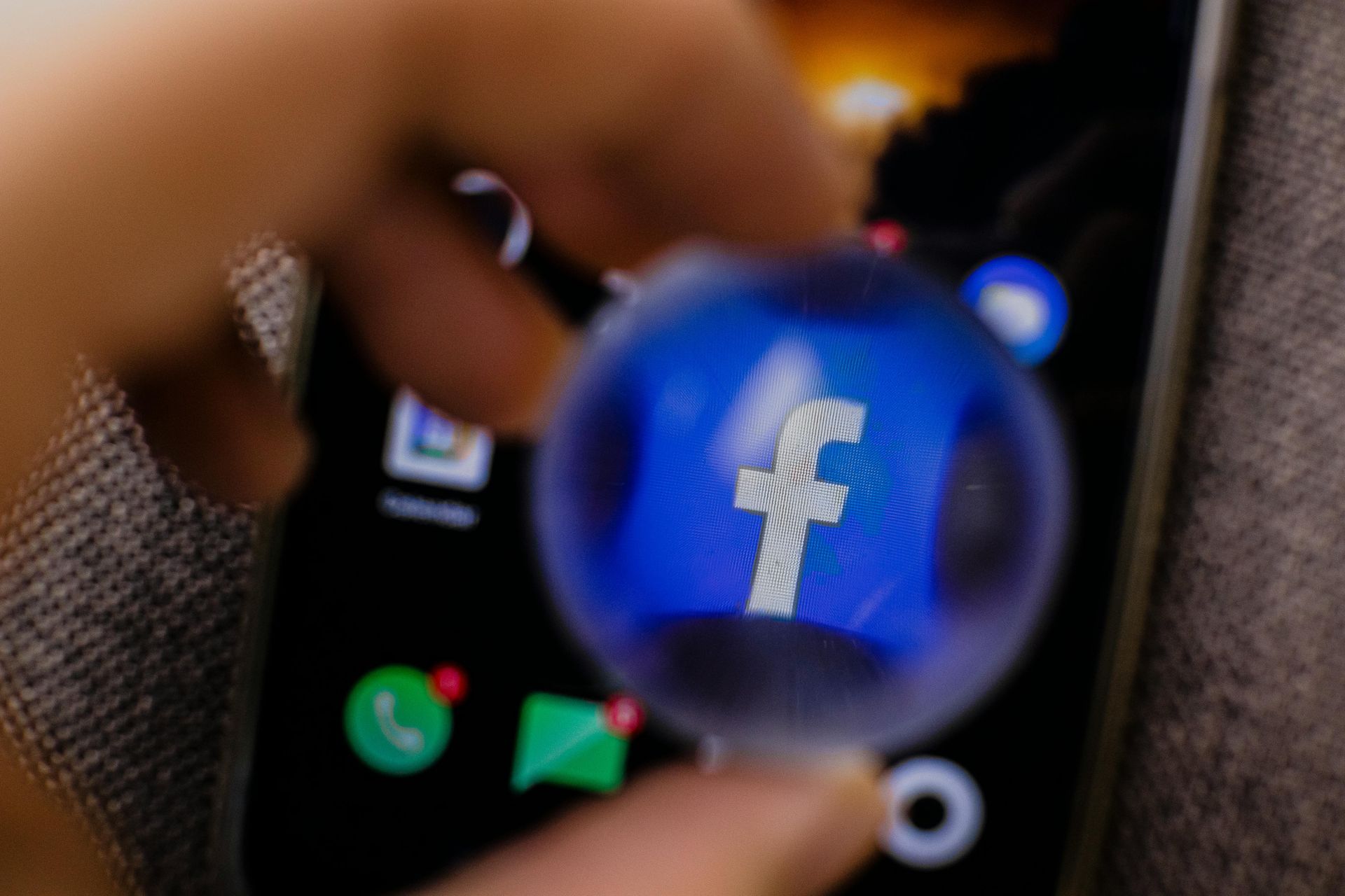 Magnifying glass over Facebook icon on a smartphone screen