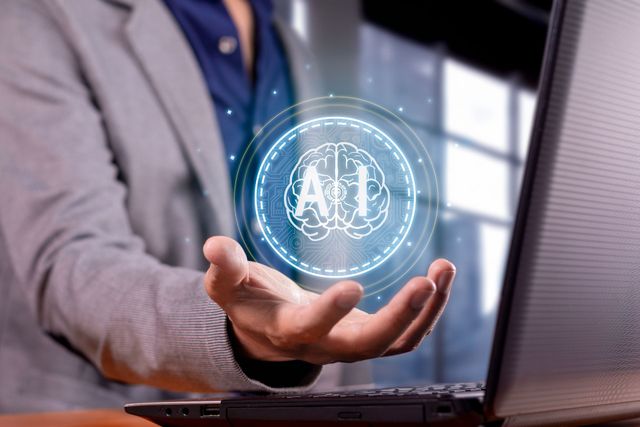 A man is holding a virtual brain in front of a laptop computer.