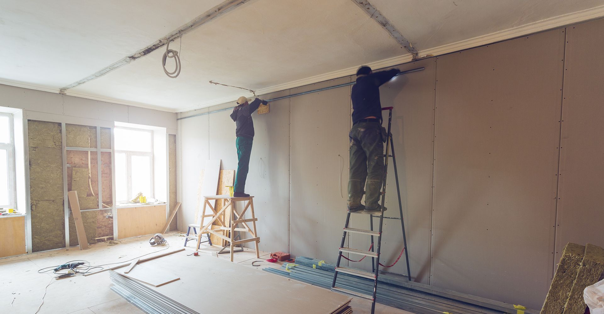Two men are working on a wall in a room.