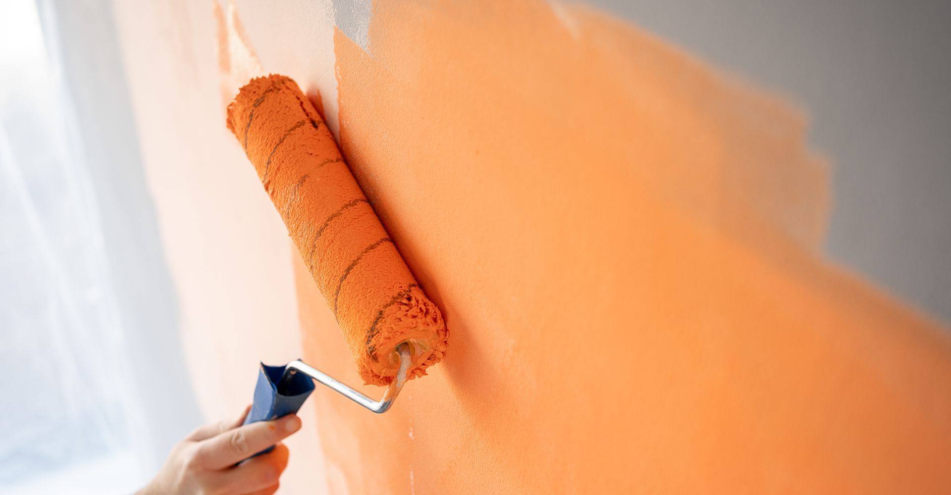 A person is painting a wall with an orange paint roller.