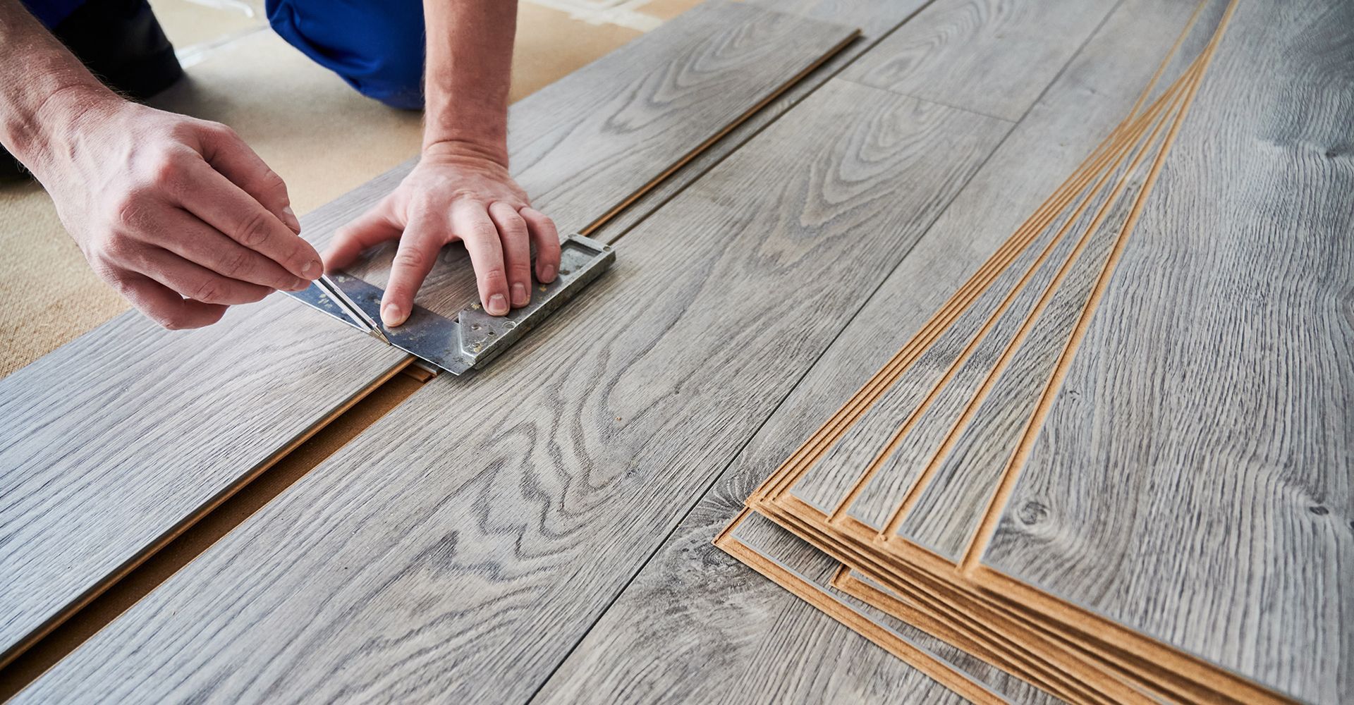 A person is installing a wooden floor with a spatula.