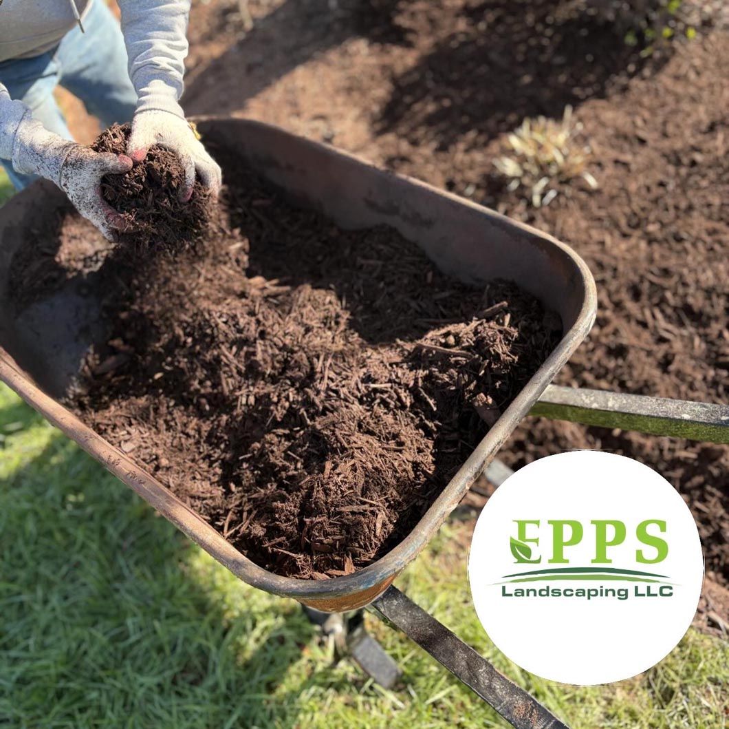 Hands spreading dark mulch in a wheelbarrow beside an EPPS Landscaping LLC logo