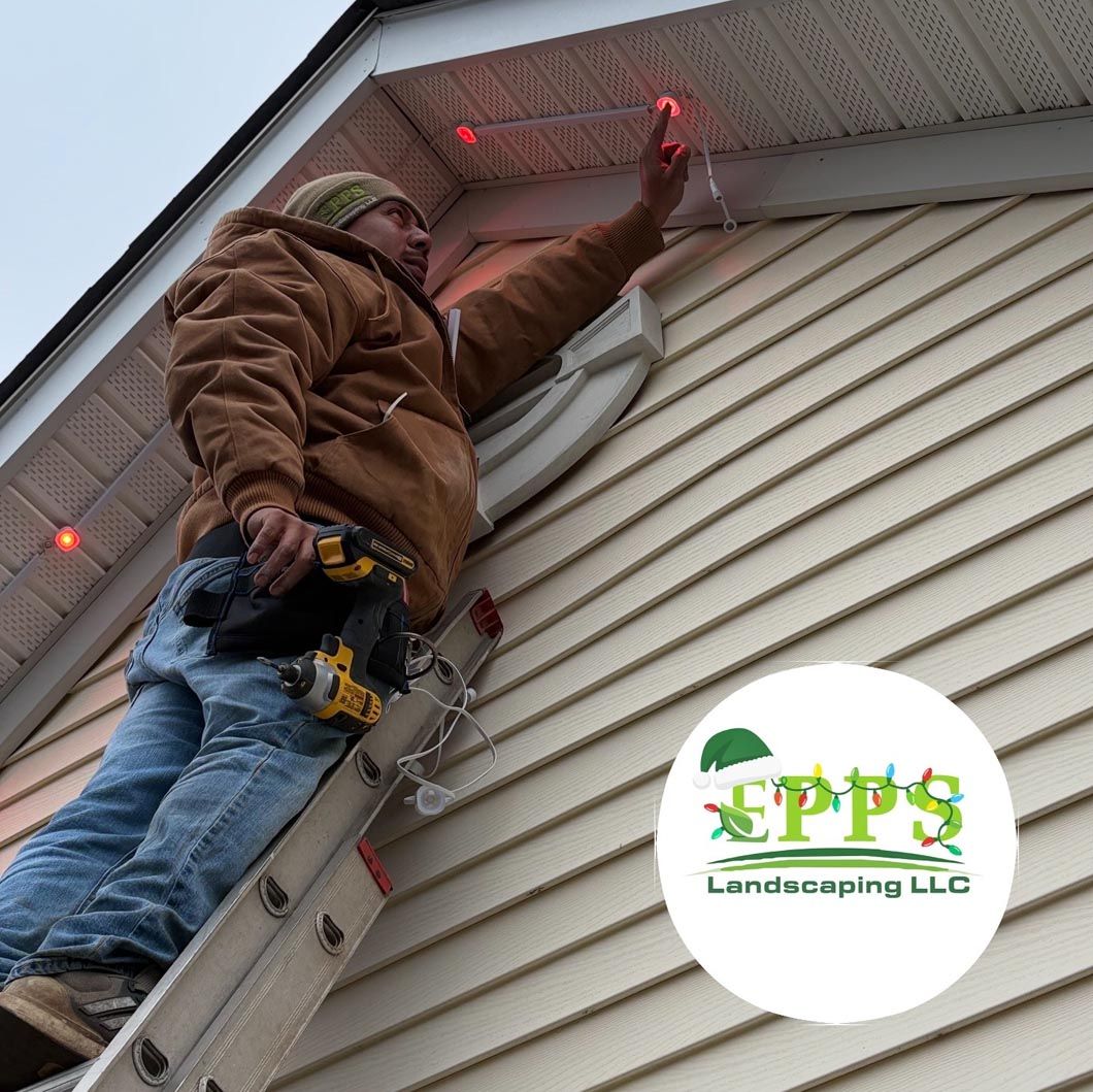 Worker installing holiday lights on a house roofline with a ladder; EPPS Landscaping LLC logo in corner