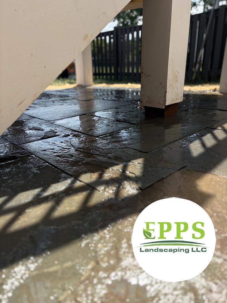 Wet tiled patio under stairs with sunlight and shadows, fenced yard in the background, EPPS logo watermark.