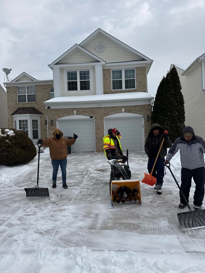 People shoveling a snowy driveway in front of a house after a heavy snowfall
