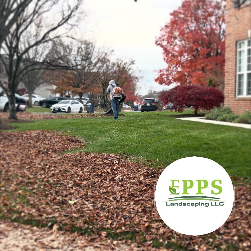 Landscaping crew blowing leaves on a lawn beside a brick building in autumn.