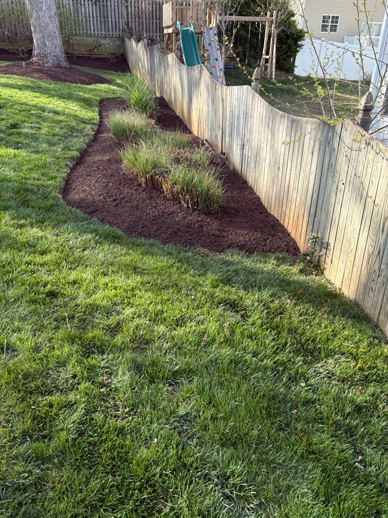 Backyard lawn with a mulched garden bed along a fence in bright sunlight