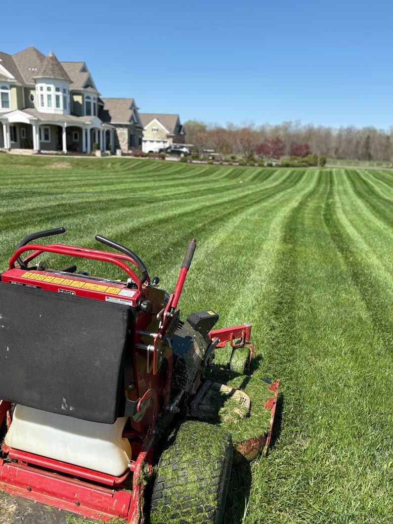 Red lawn mower on a striped green lawn beside a large house on a clear day