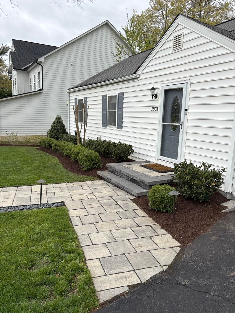 White house exterior with stone walkway, steps, small front porch, and landscaped lawn and shrubs