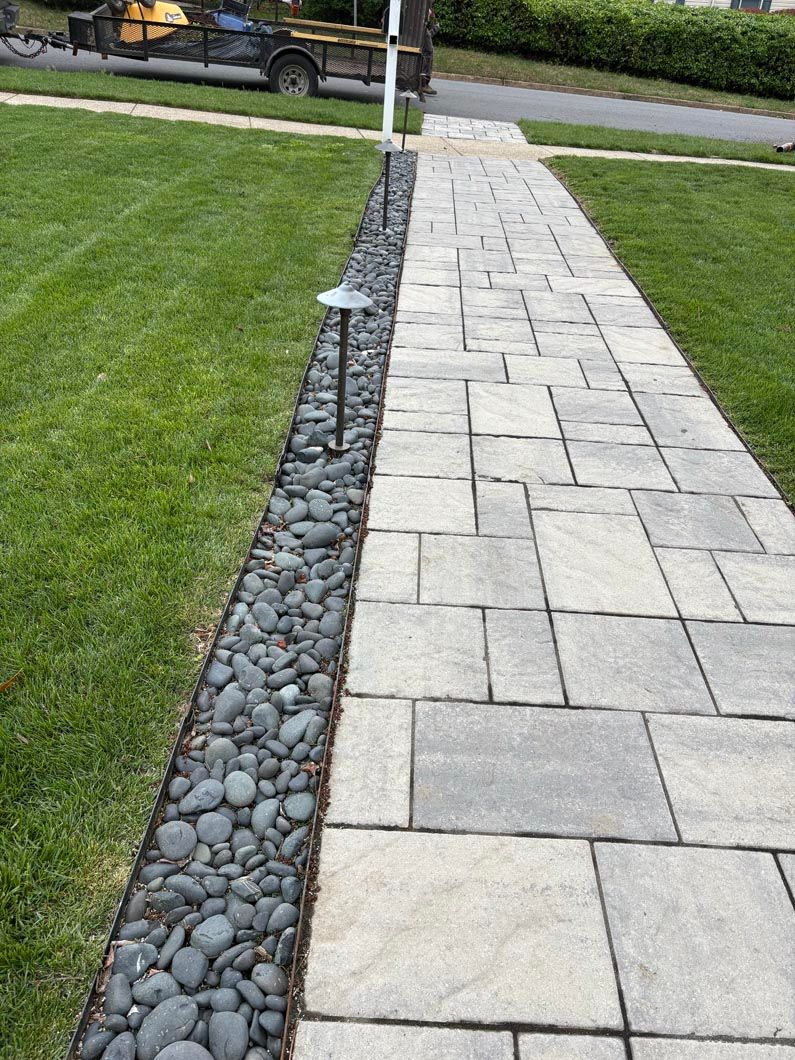 Stone walkway beside a green lawn, edged with decorative gravel and leading toward a street.