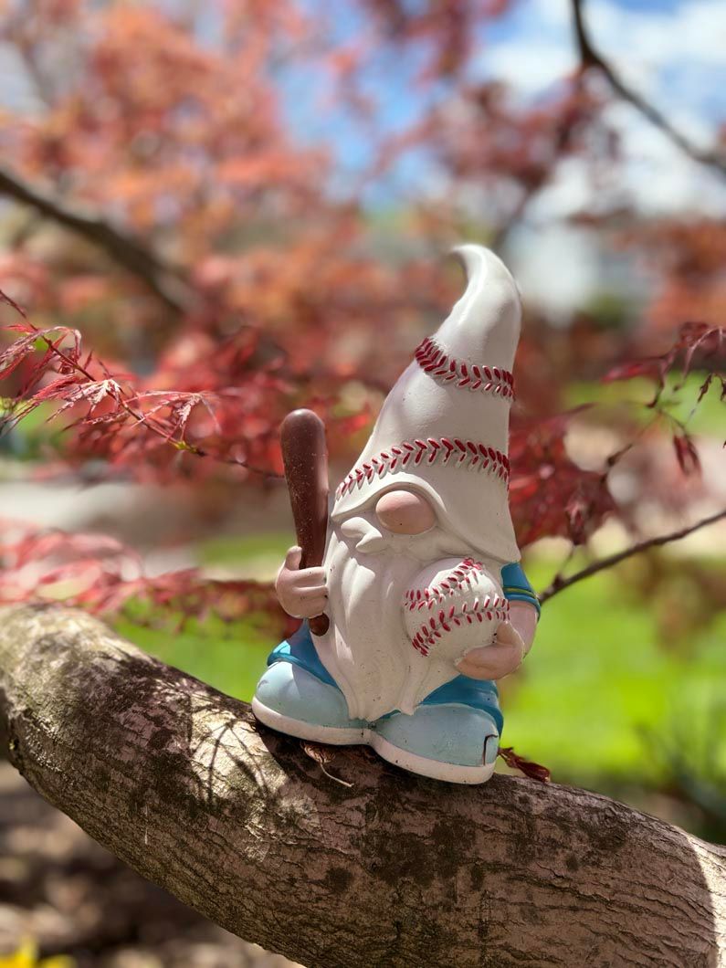 Small garden gnome with blue shoes sitting on a tree branch among blurred pink blossoms