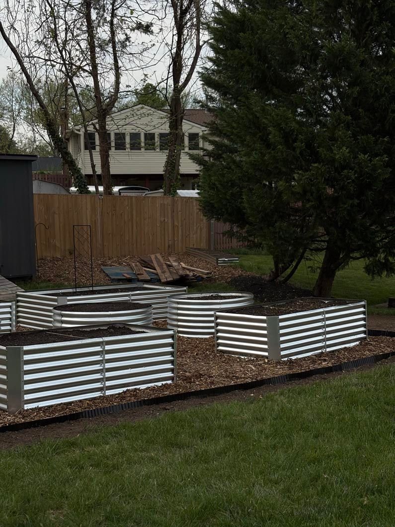 Corrugated metal raised garden beds in a backyard with trees, fence, and grass.
