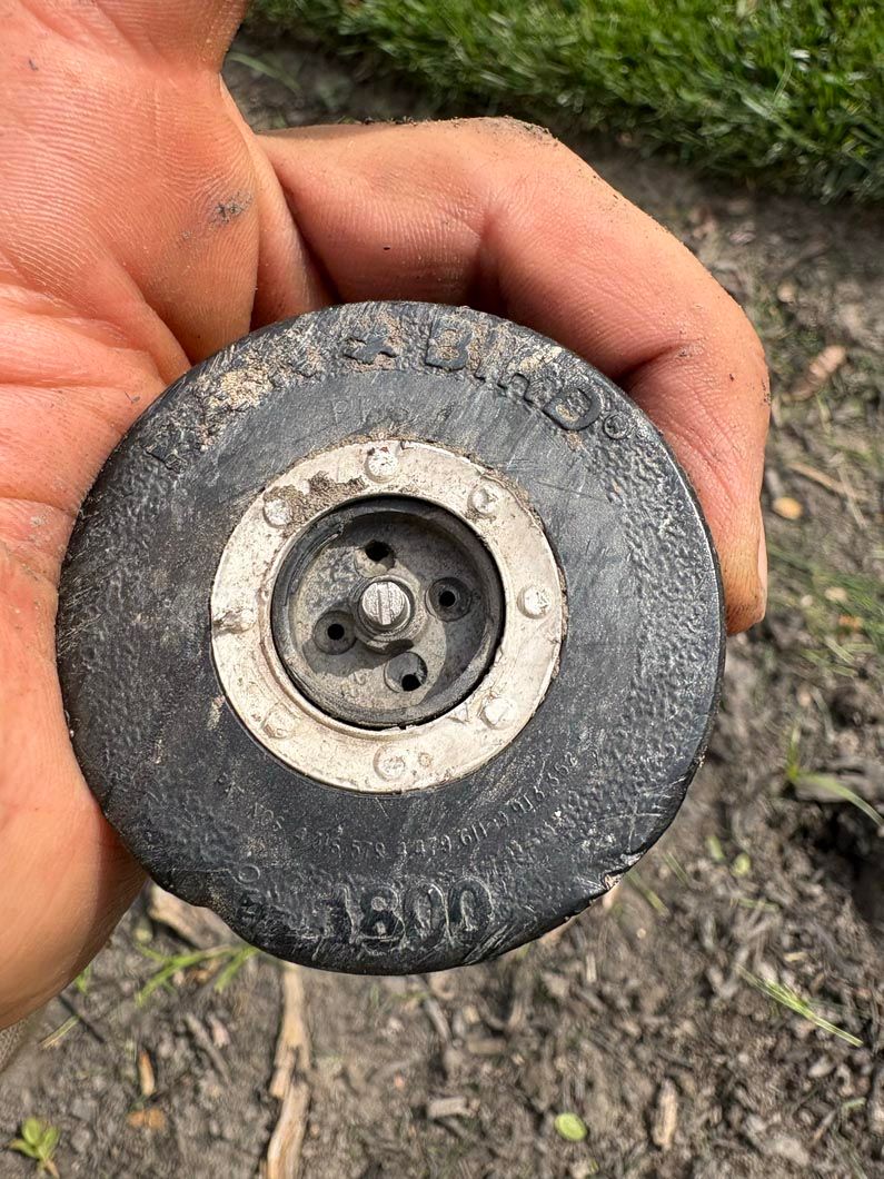 Close-up of a hand holding a worn black wheel with a metal hub on the ground