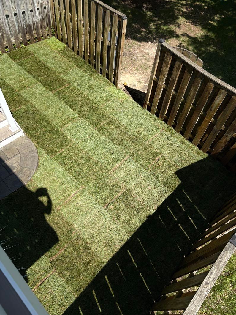 Wooden deck with green artificial turf and railings, viewed from above.