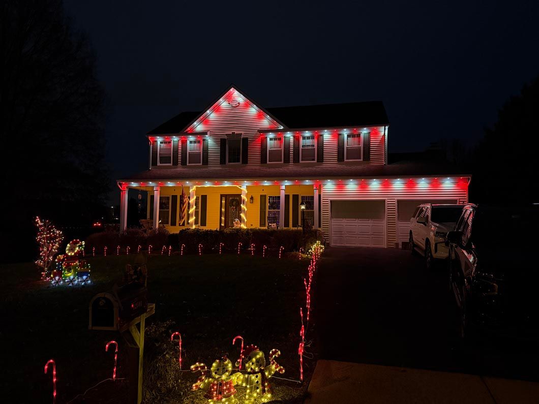House decorated with red and white Christmas lights at night, with glowing yard decorations and a lit porch