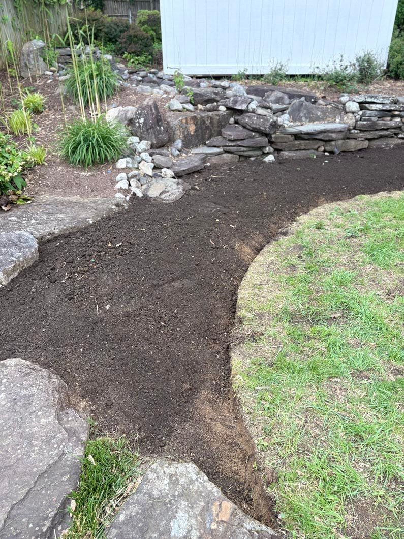 Fresh dark mulch covers a curved garden bed beside rocks and green grass near a stone retaining wall.