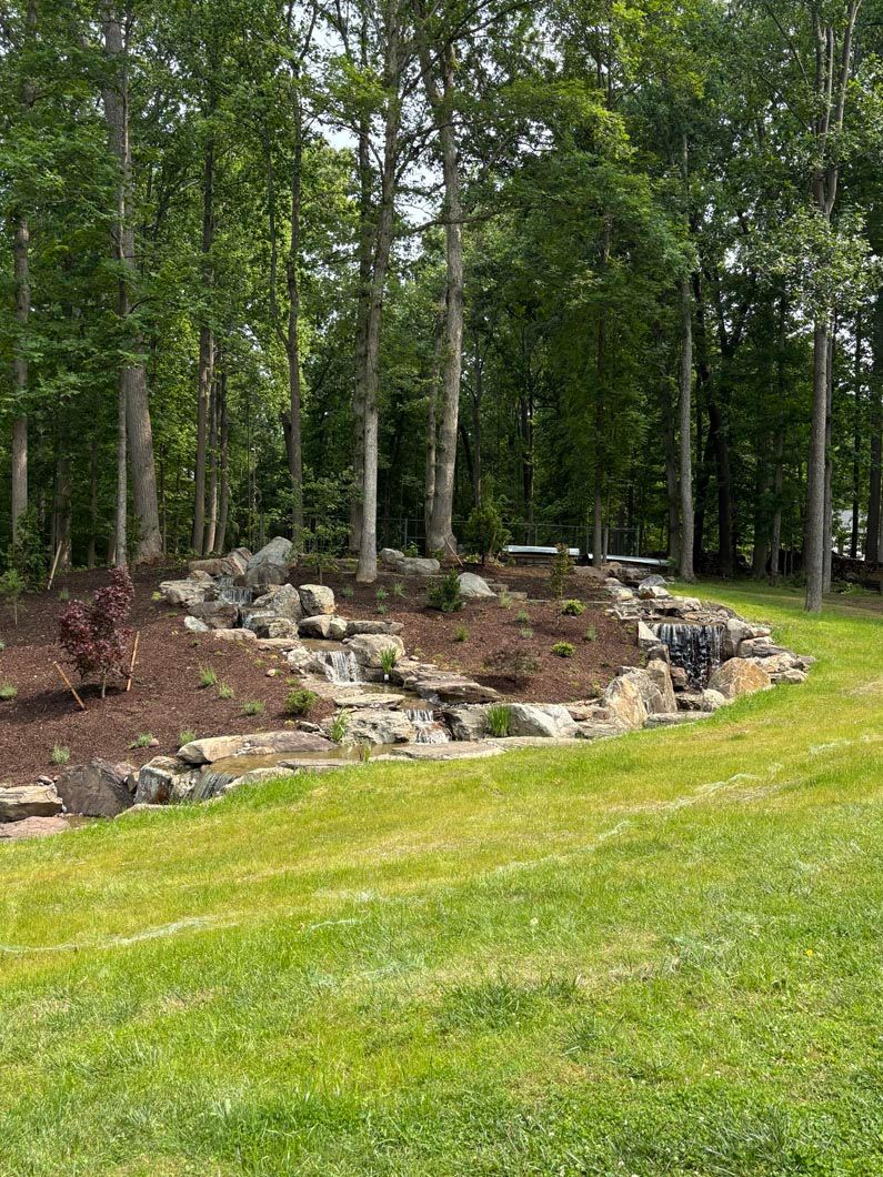 Rocky landscaped bed with mulch and trees beside a green lawn in a wooded area