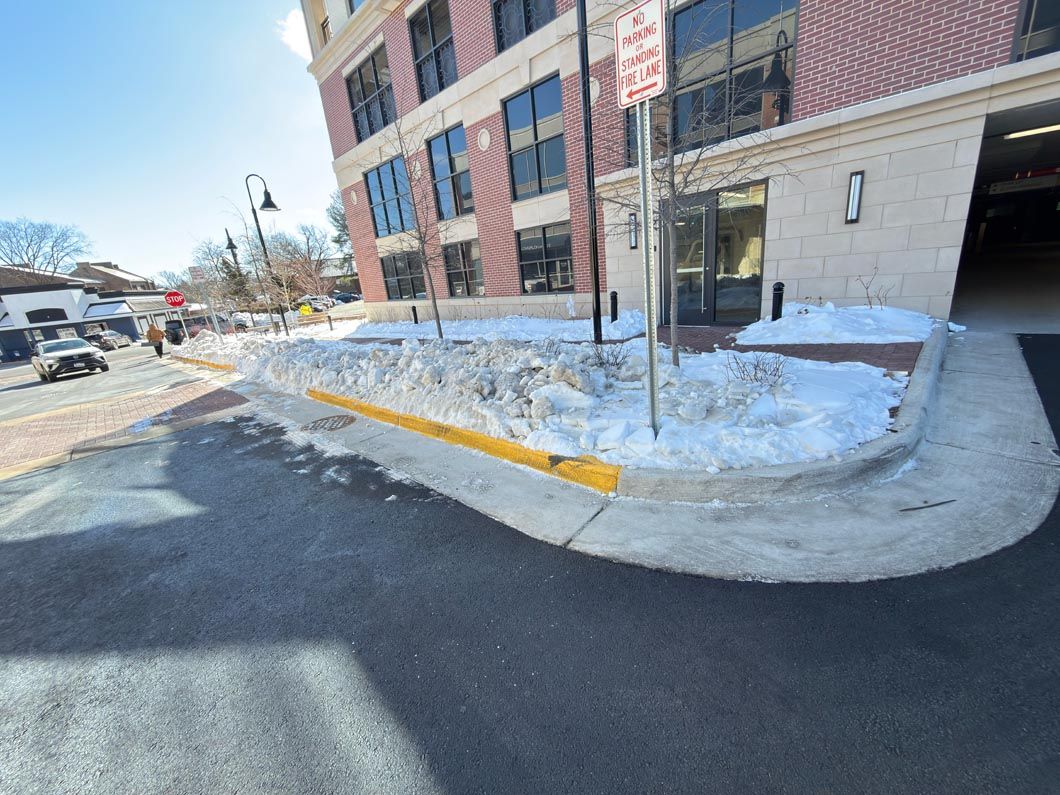 Snowy apartment entrance with a curb ramp and yellow-painted curb beside a parking lot