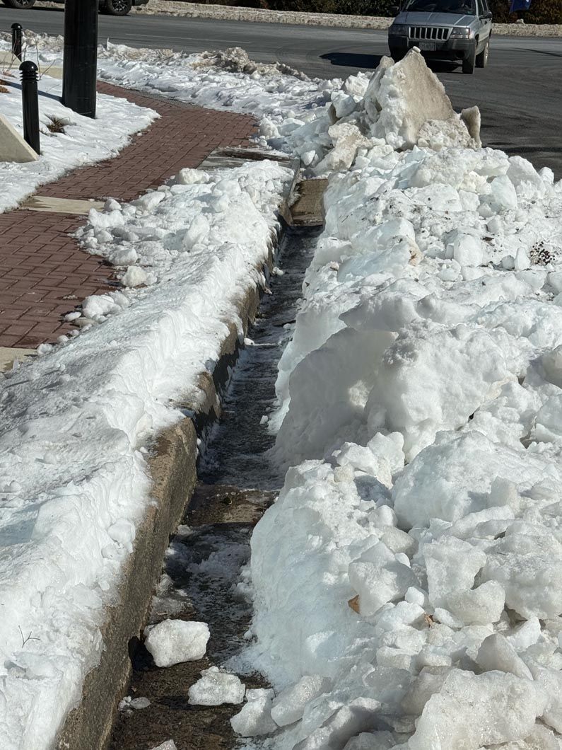 Snowy sidewalk with a narrow cleared path and piled snow beside a brick walkway and street