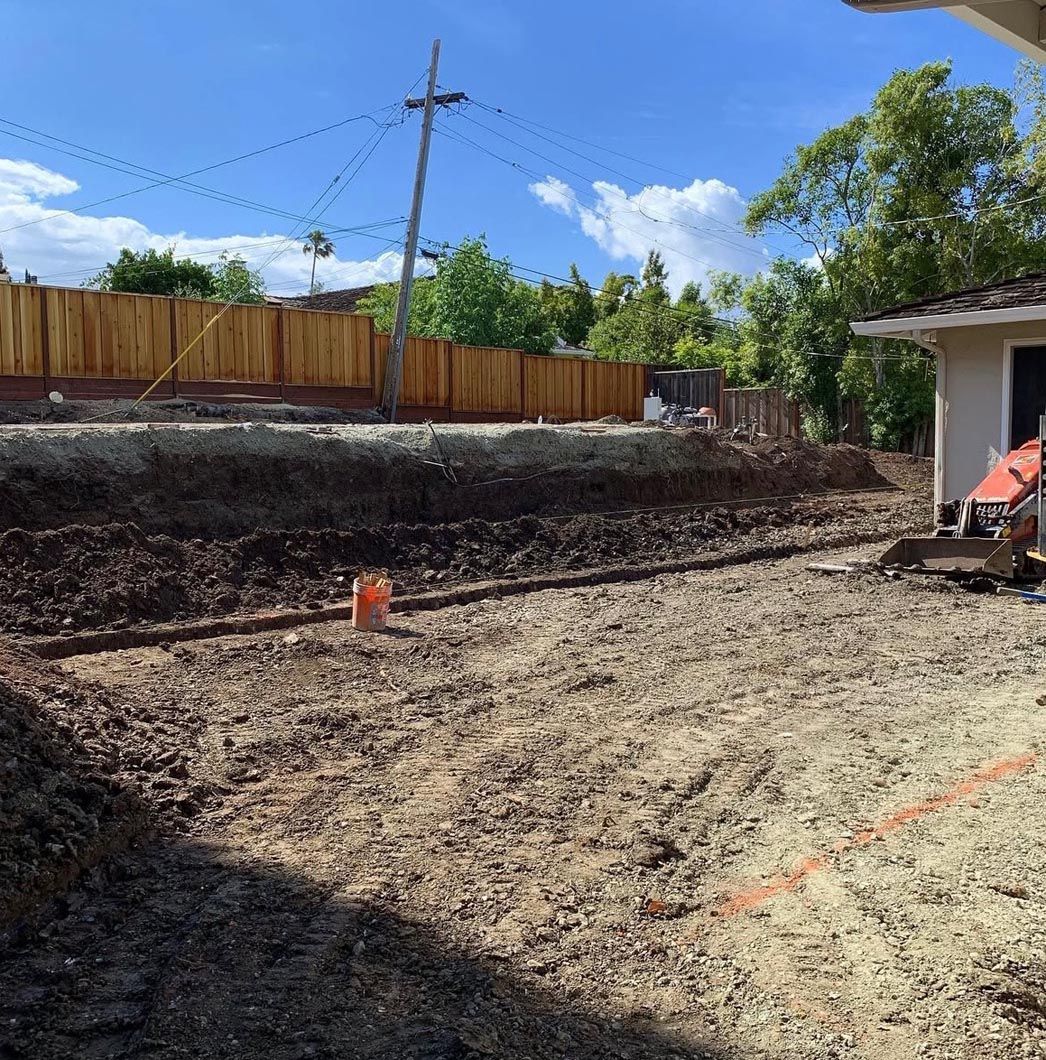 Backyard excavation site with dirt pit, wooden fence, utility pole, and a house at right
