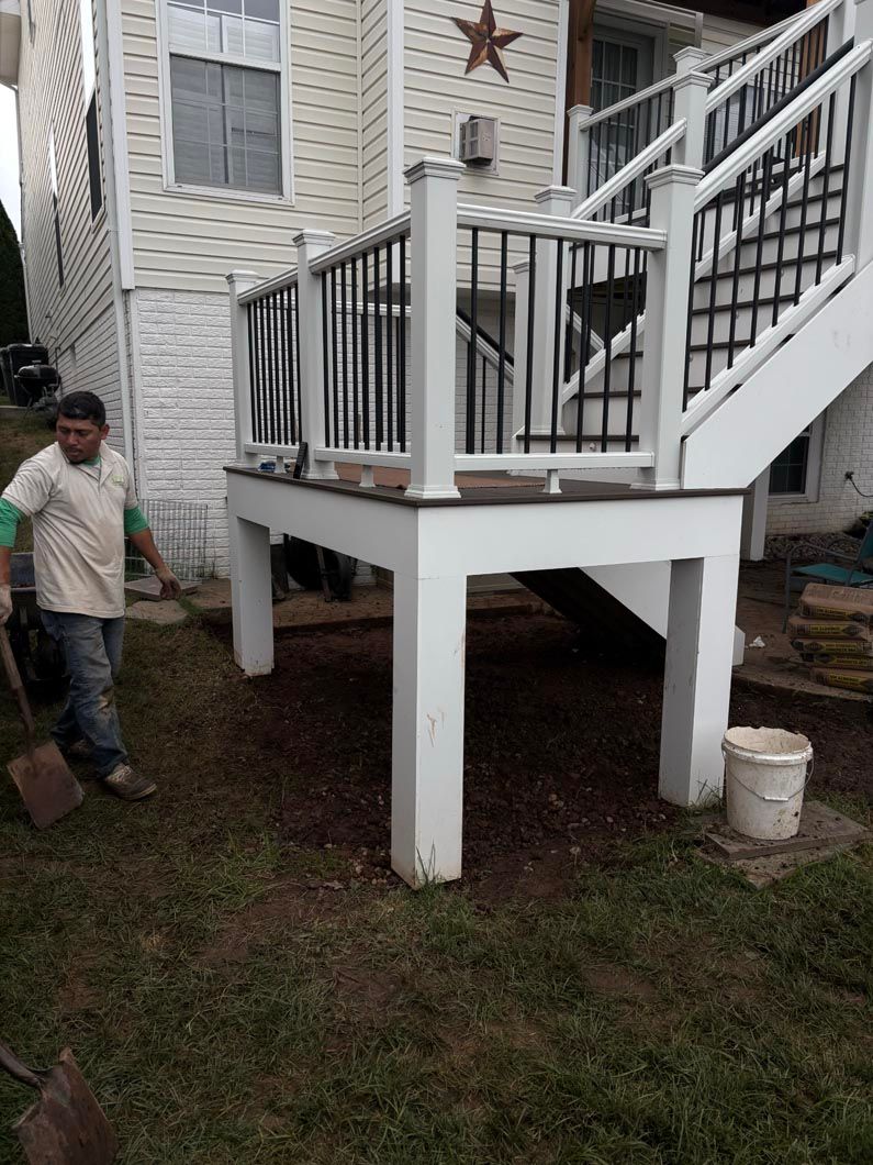 Raised white porch with stairs and black railings beside a house, with a person standing on the left.