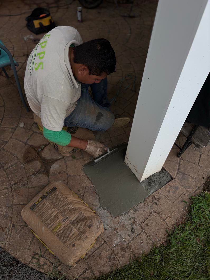 Worker applying concrete around a white post in a tiled outdoor area