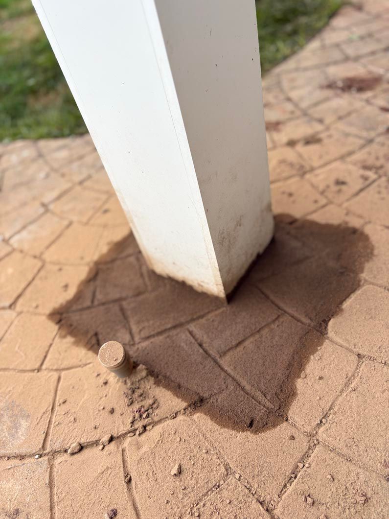 White post on brick paving with a small mound of sand at the base.