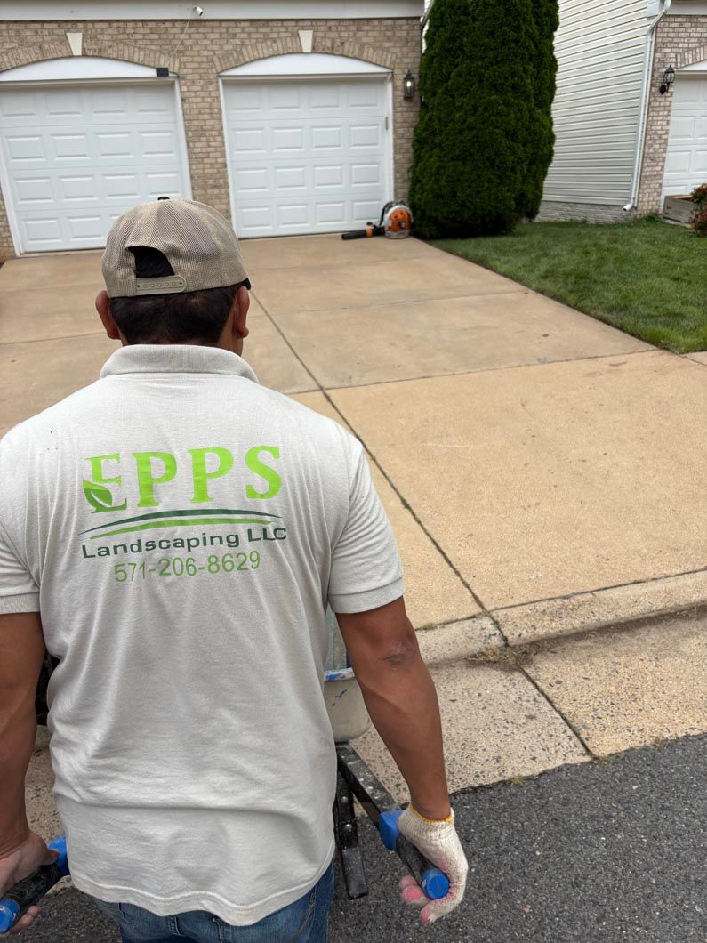 Worker in gray EPPS shirt walking on a driveway beside garage doors, holding tools.