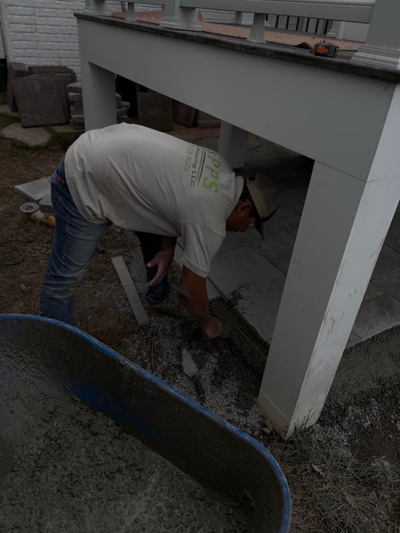 Worker bent under a raised structure, shoveling gravel at a construction site.