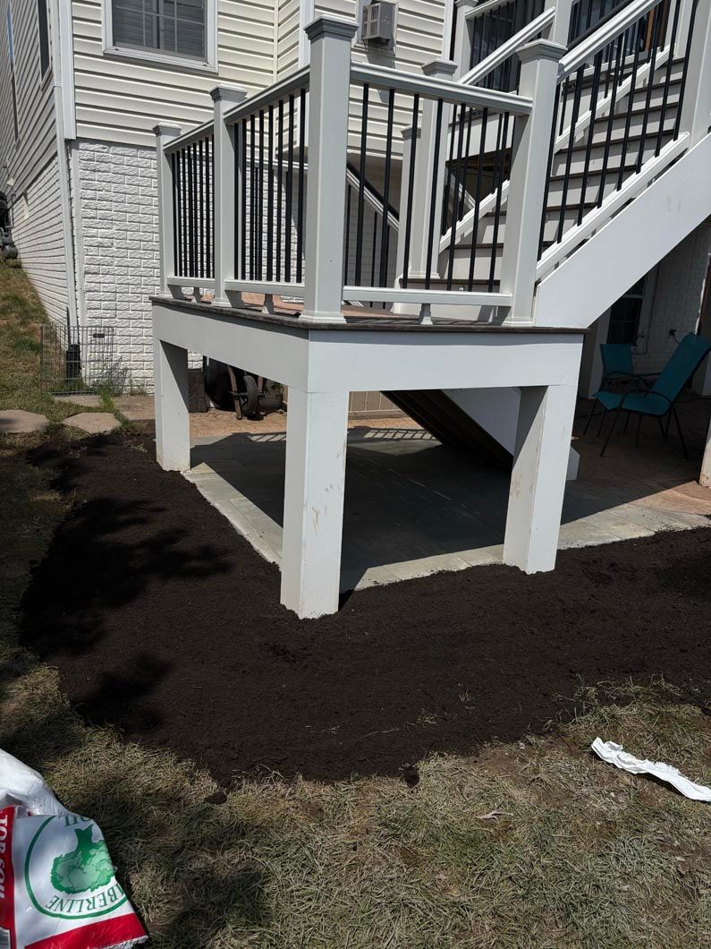 White wooden deck with black railings beside a house, above newly spread dark soil in a backyard.