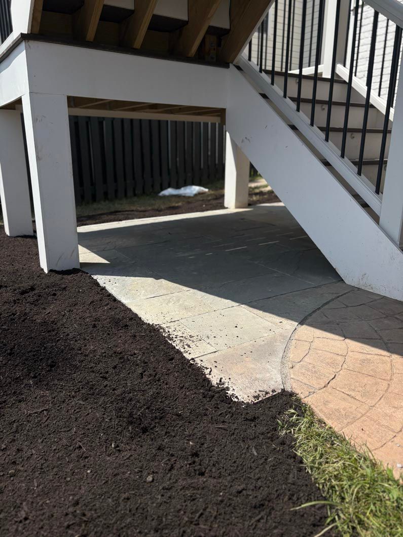 Concrete walkway under outdoor stairs beside a gravel path and grass strip