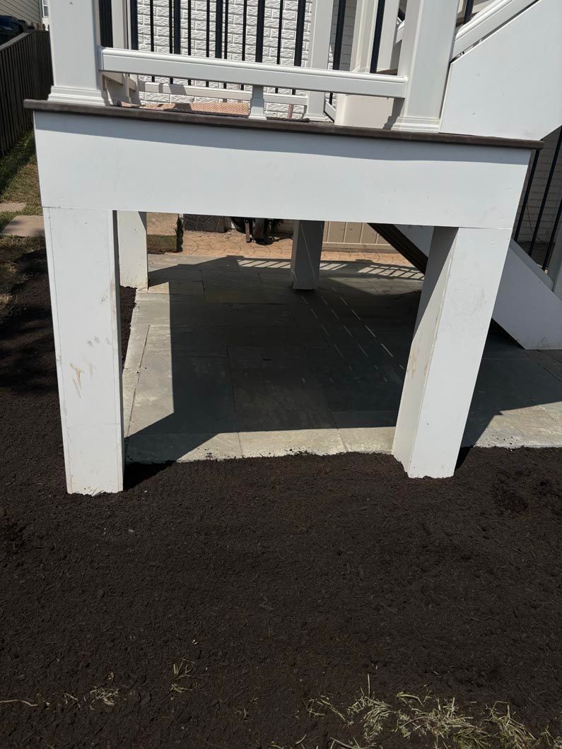 White outdoor chair or bench with thick legs on pavement, seen from the front, casting shadows.
