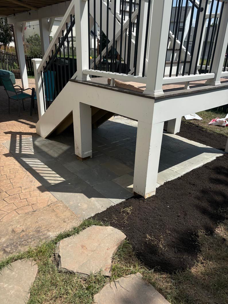White porch deck with stairs, black railing, and a concrete pad bordered by mulch and stepping stones.