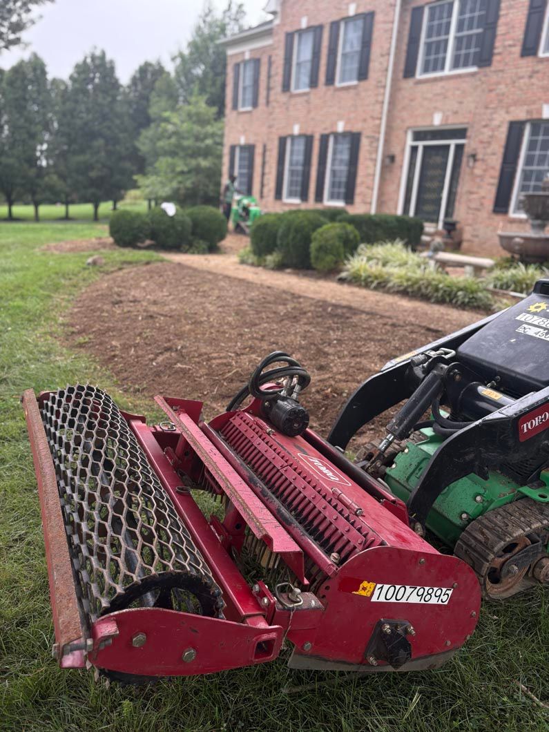 Red skid-steer loader with brush mower attachment on a lawn beside a brick building