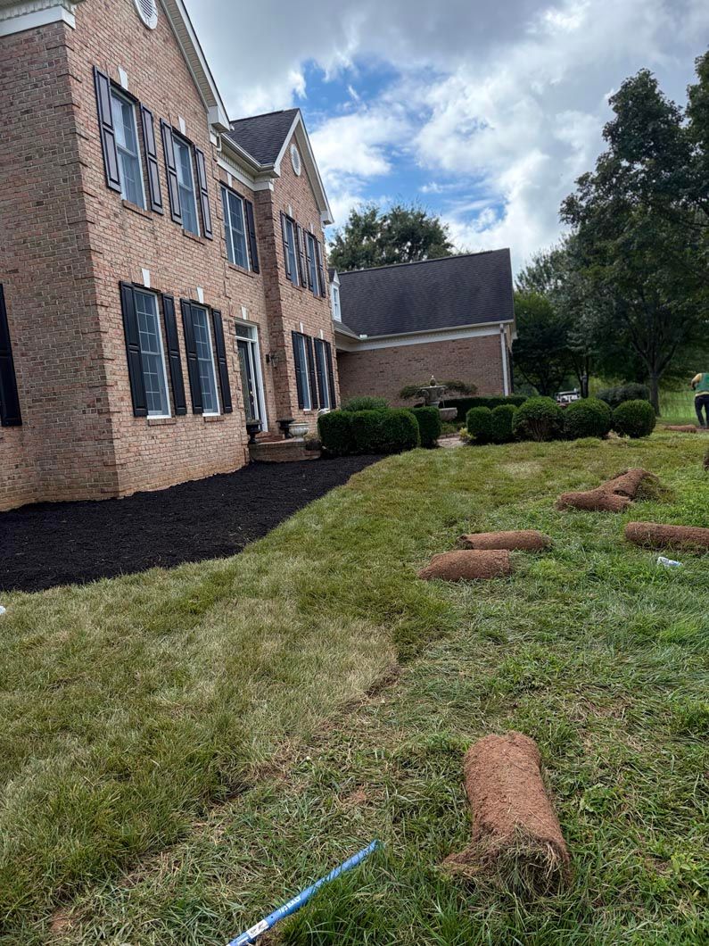 Brick house beside a grassy yard with scattered logs and a cloudy sky