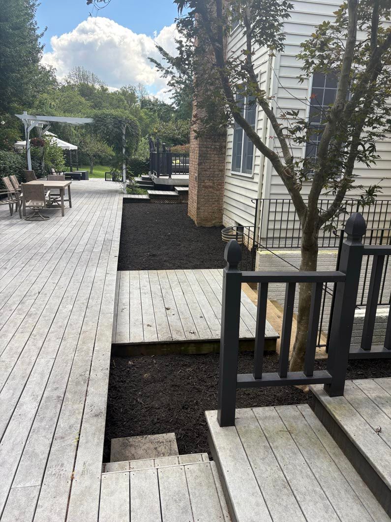 Wooden deck with steps, black railings, and a gravel path beside a white house under a cloudy sky