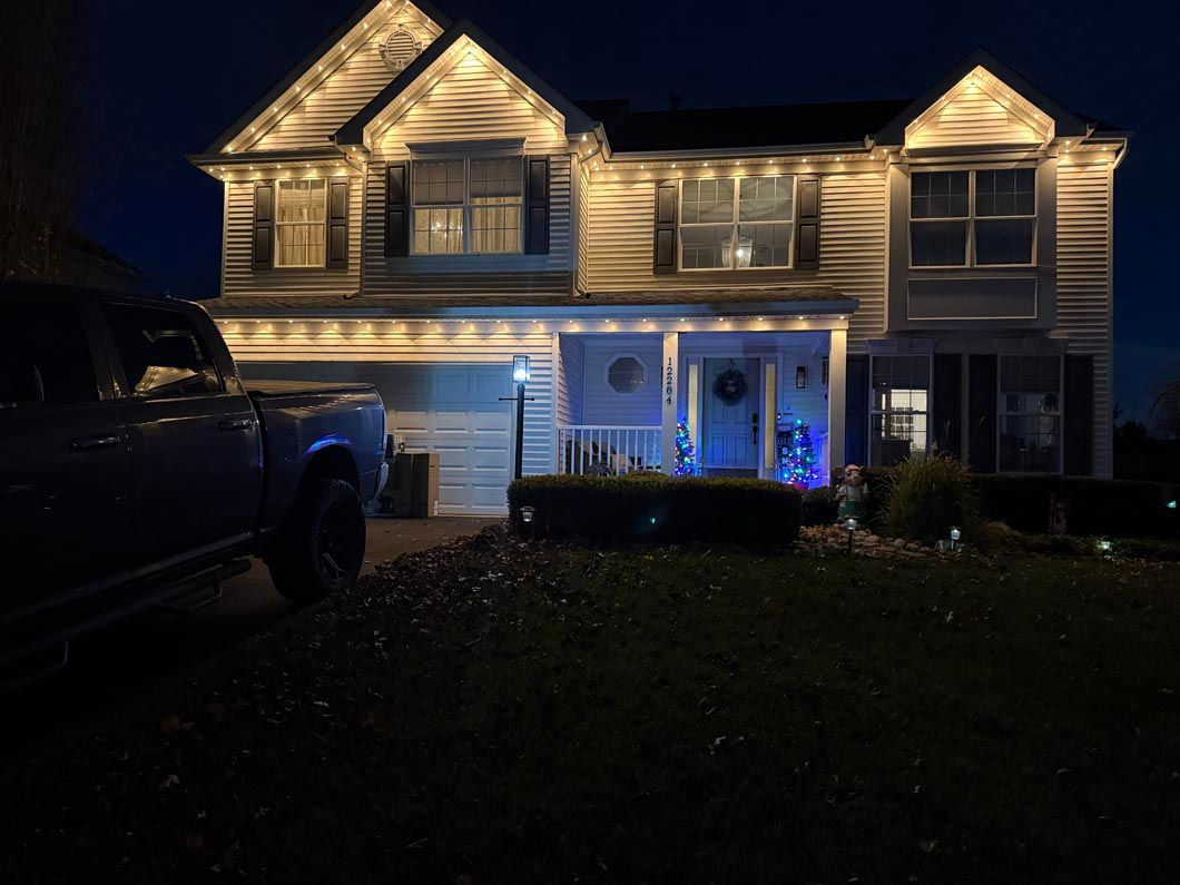 Two-story house at night with warm white and blue holiday lights and a truck parked in the driveway