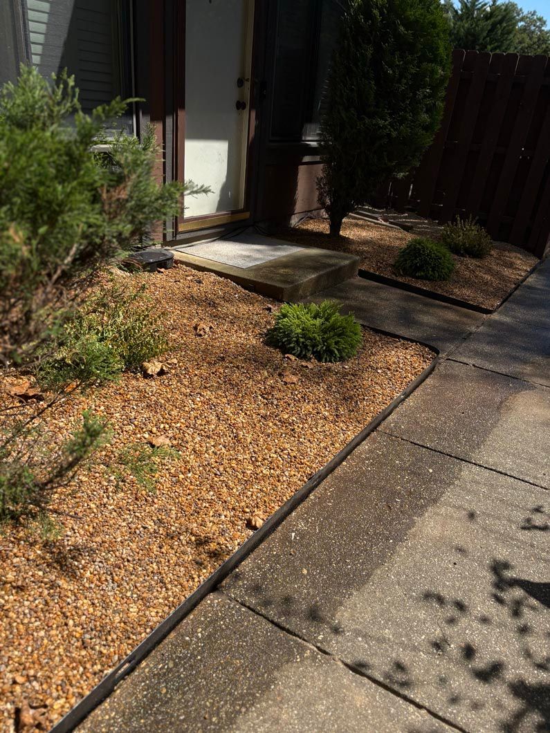 Front yard with gravel landscaping, small shrubs, and a concrete walkway beside a house