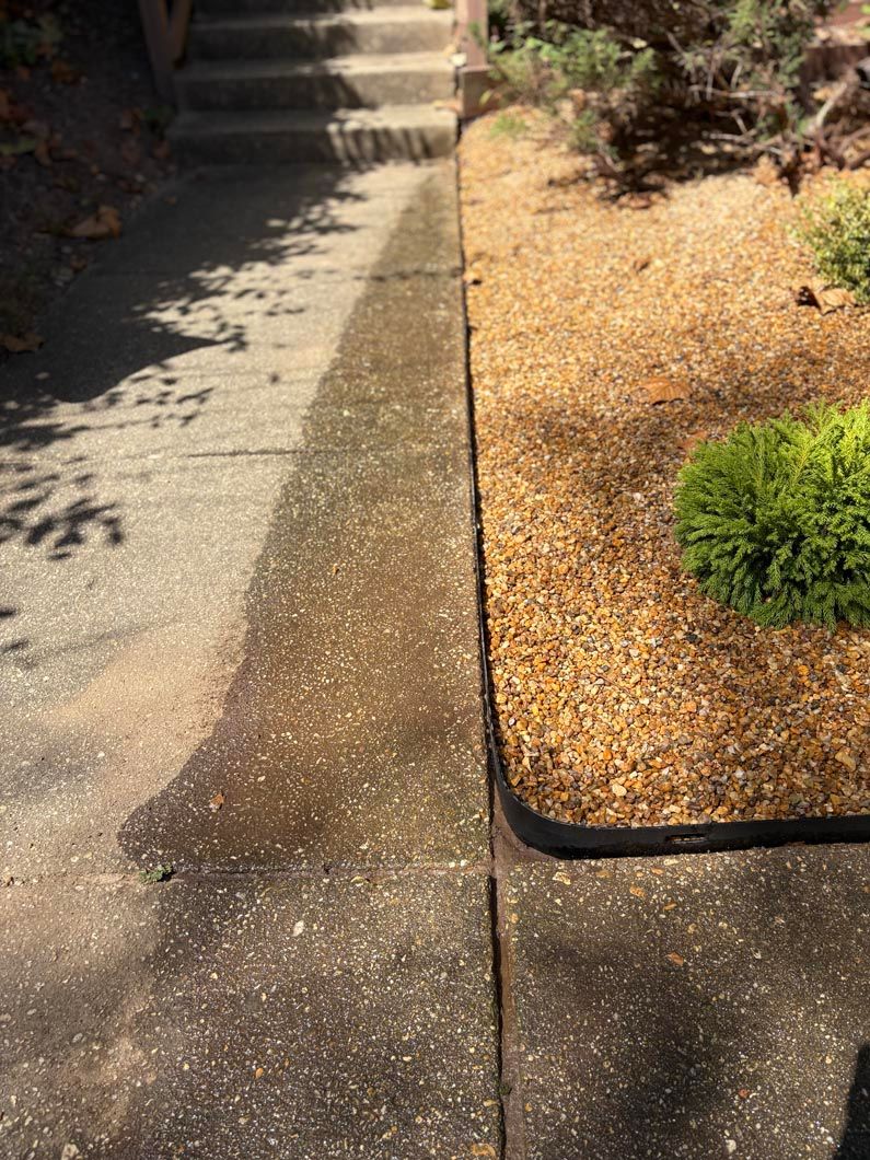 Concrete walkway beside a gravel garden bed, with stairs in the background and dappled sunlight.