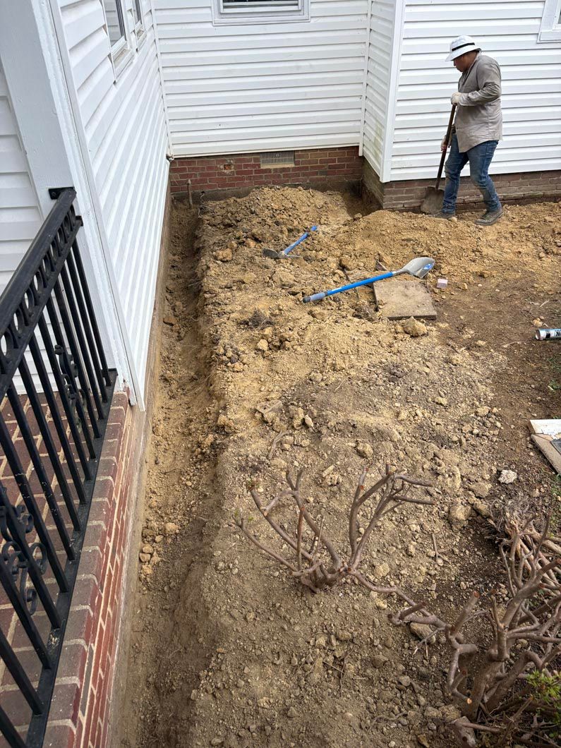 Worker standing beside a dug-up backyard trench near a white house and black fence