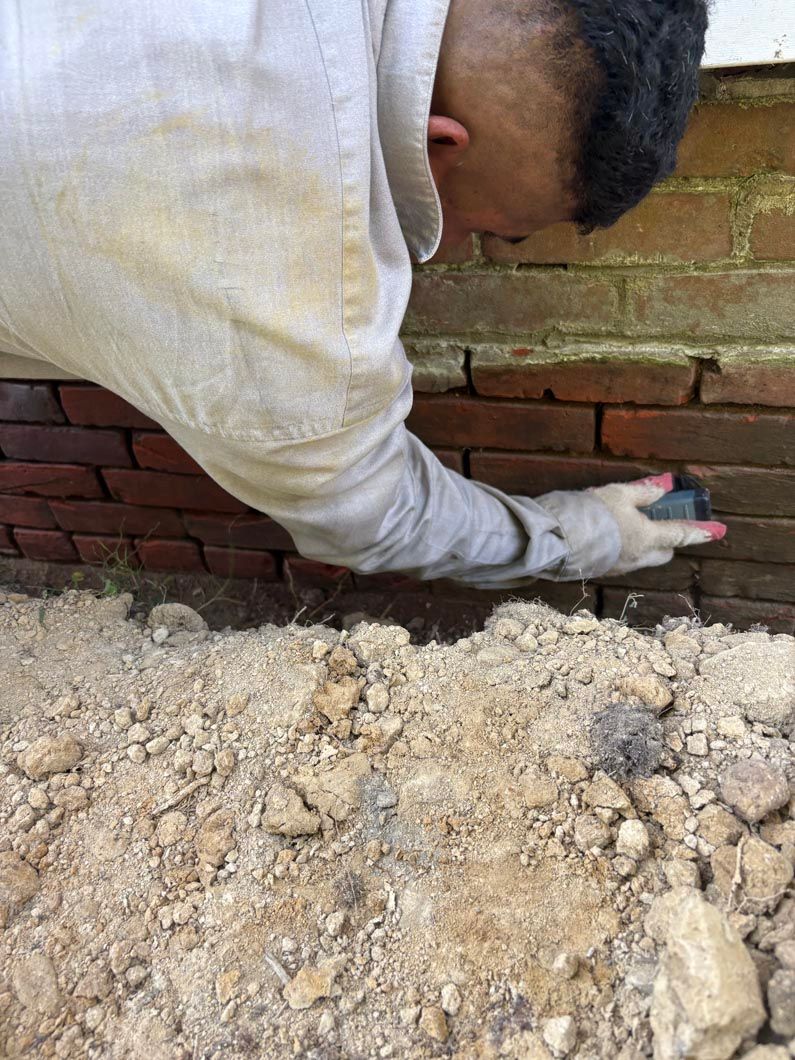 Person in a light shirt using a tool to repair a brick wall near a dirt foundation