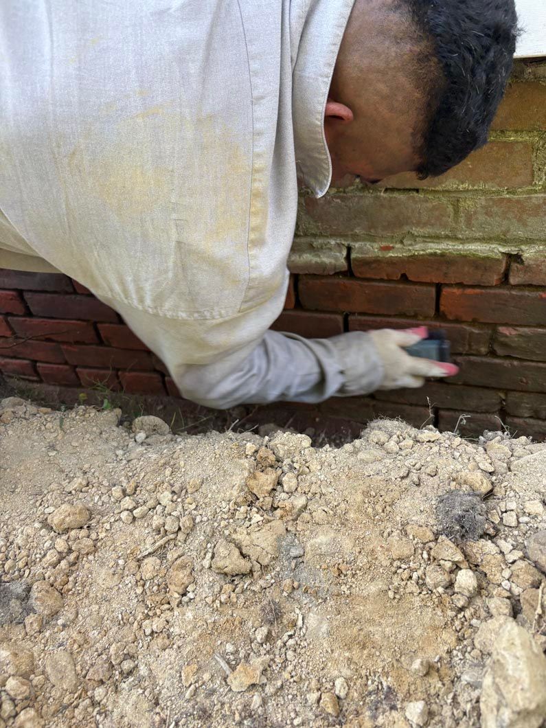 Worker troweling mortar into a brick wall crack beside a pile of debris