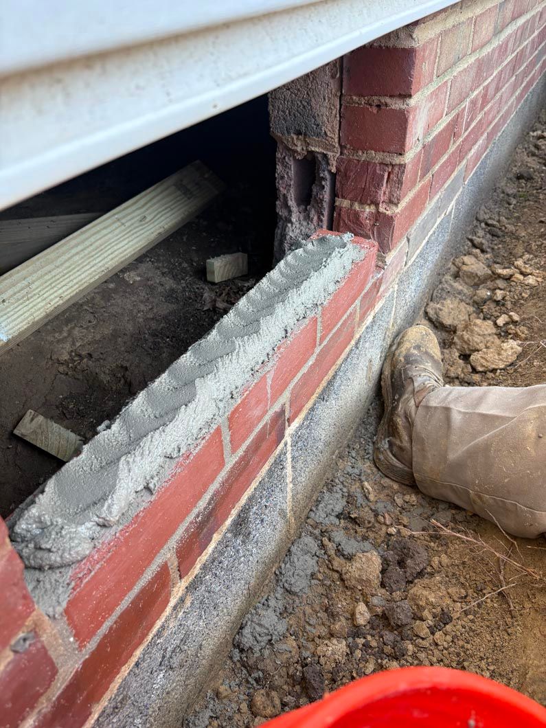 Broken brick foundation corner with exposed interior framing and dirt beside the house
