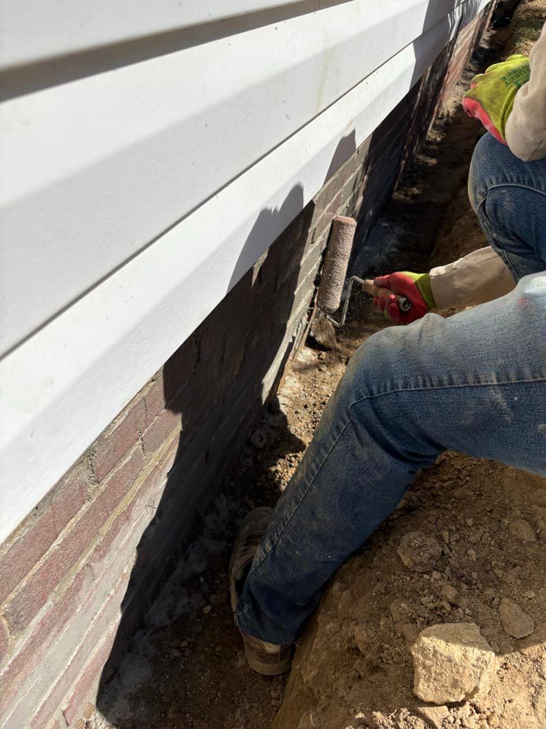 Worker repairing house foundation beside white siding with shovel and concrete patch, outdoors