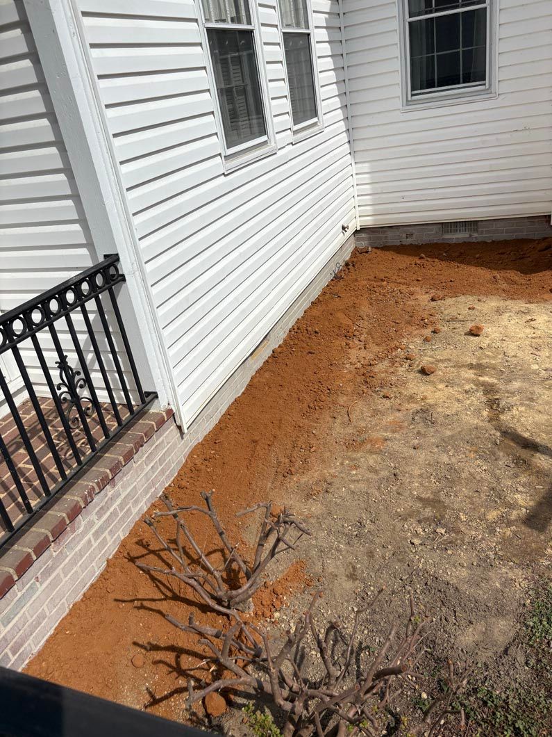 Side yard with white vinyl siding, brick foundation, windows, and bare dirt landscaping border.