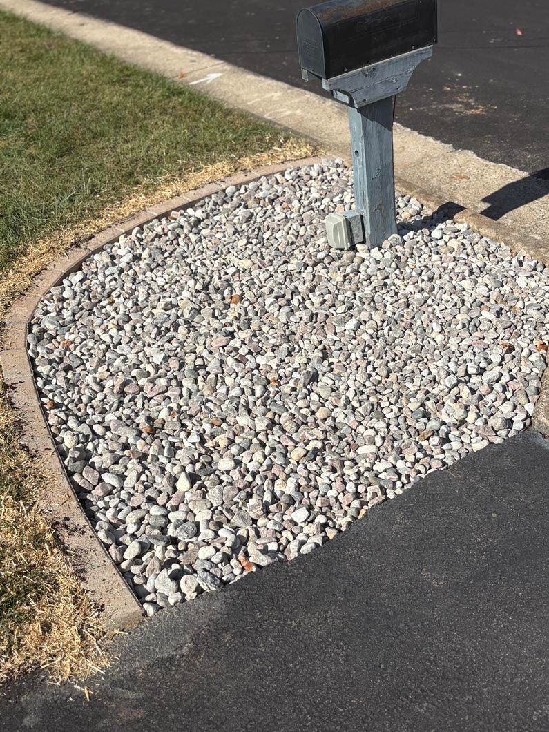 Metal mailbox beside a driveway, surrounded by a gravel bed with a concrete border
