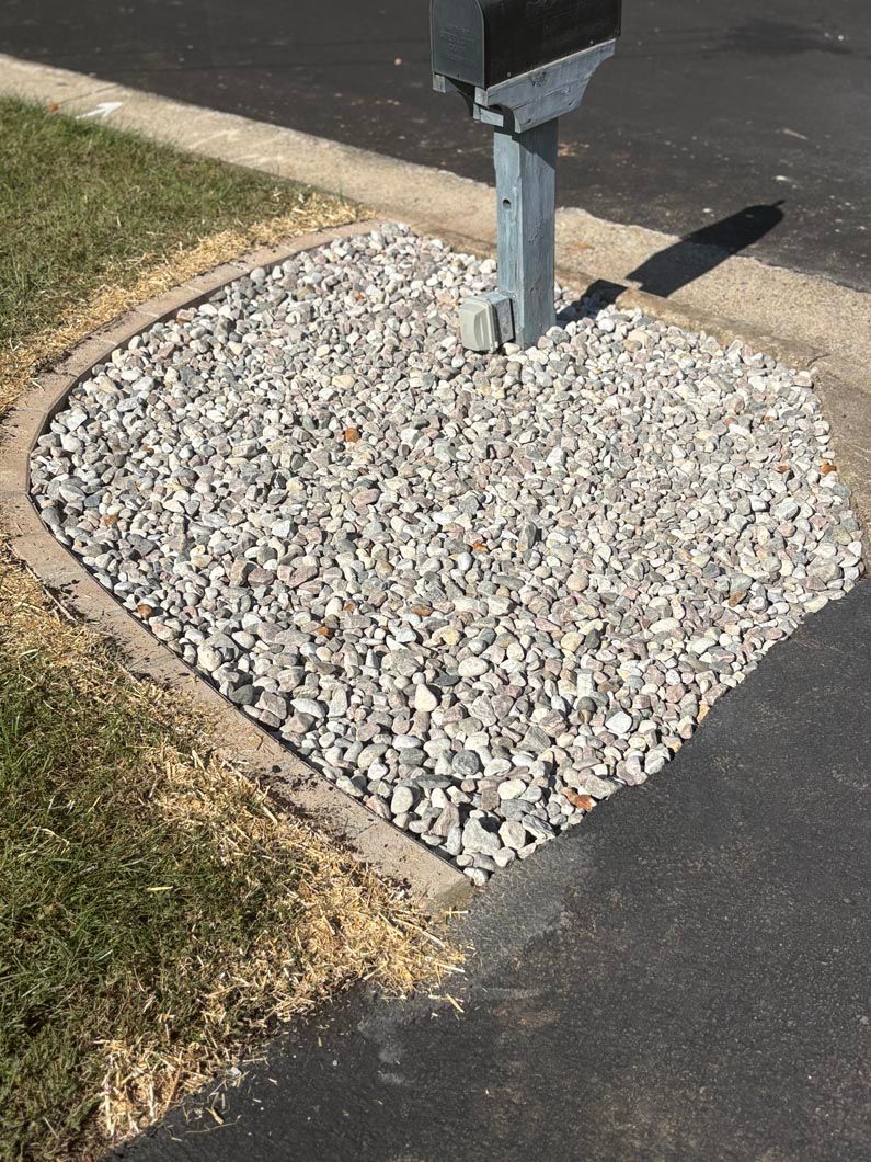 Mailbox post on a gravel patch beside a curb and sidewalk.