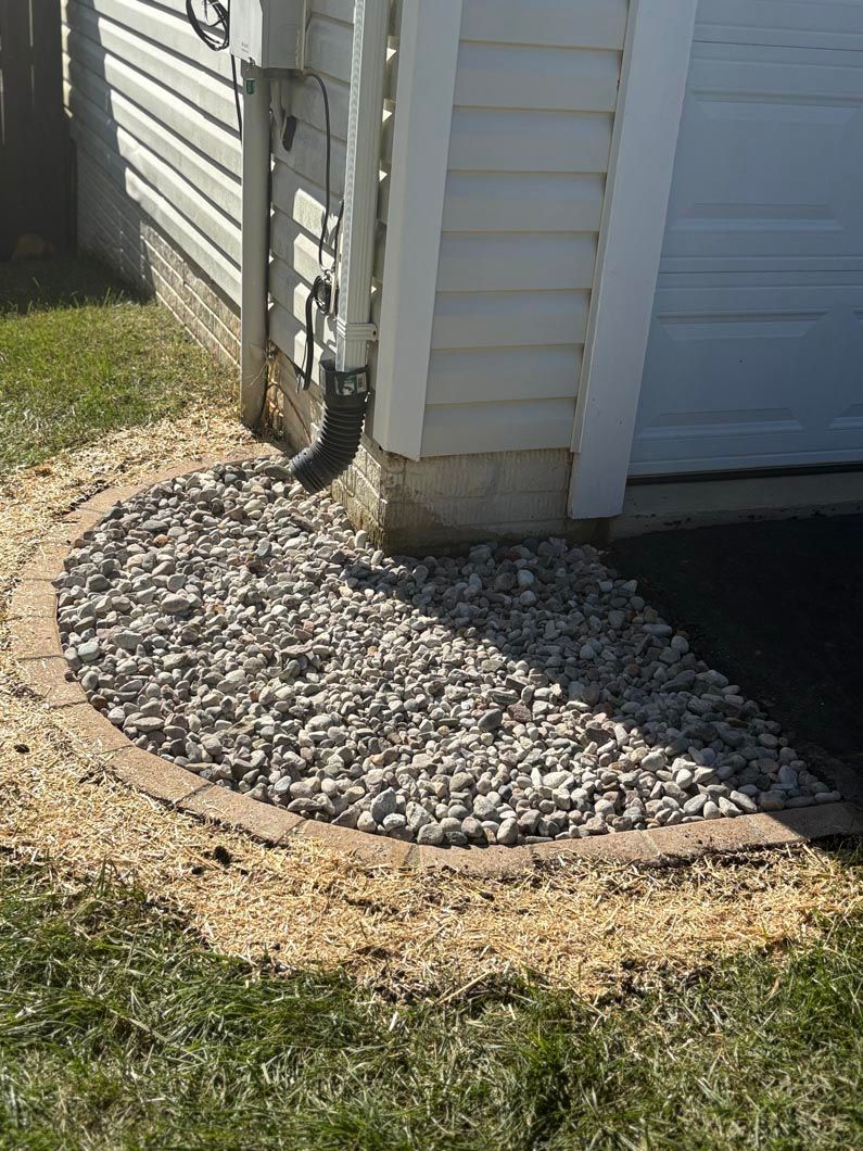 Corner of a house with gray siding, gravel drainage bed, and a dirt border along the foundation.