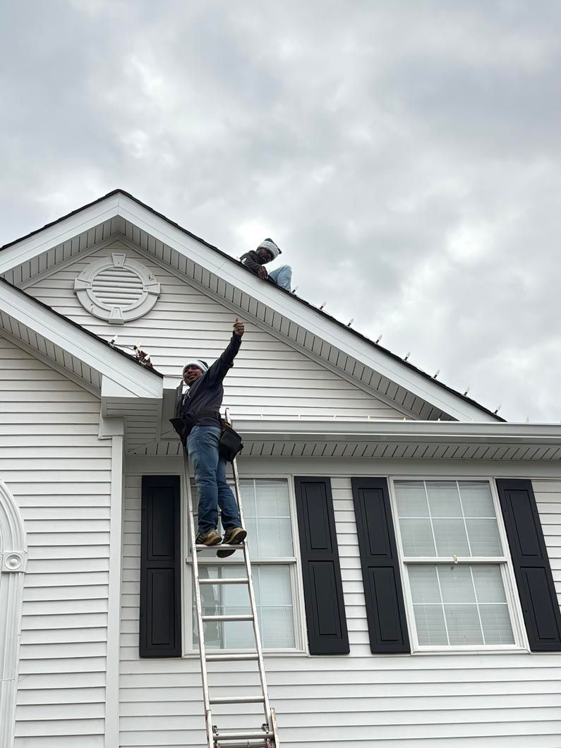 Person on a ladder painting a white house roofline while another works on the roof.