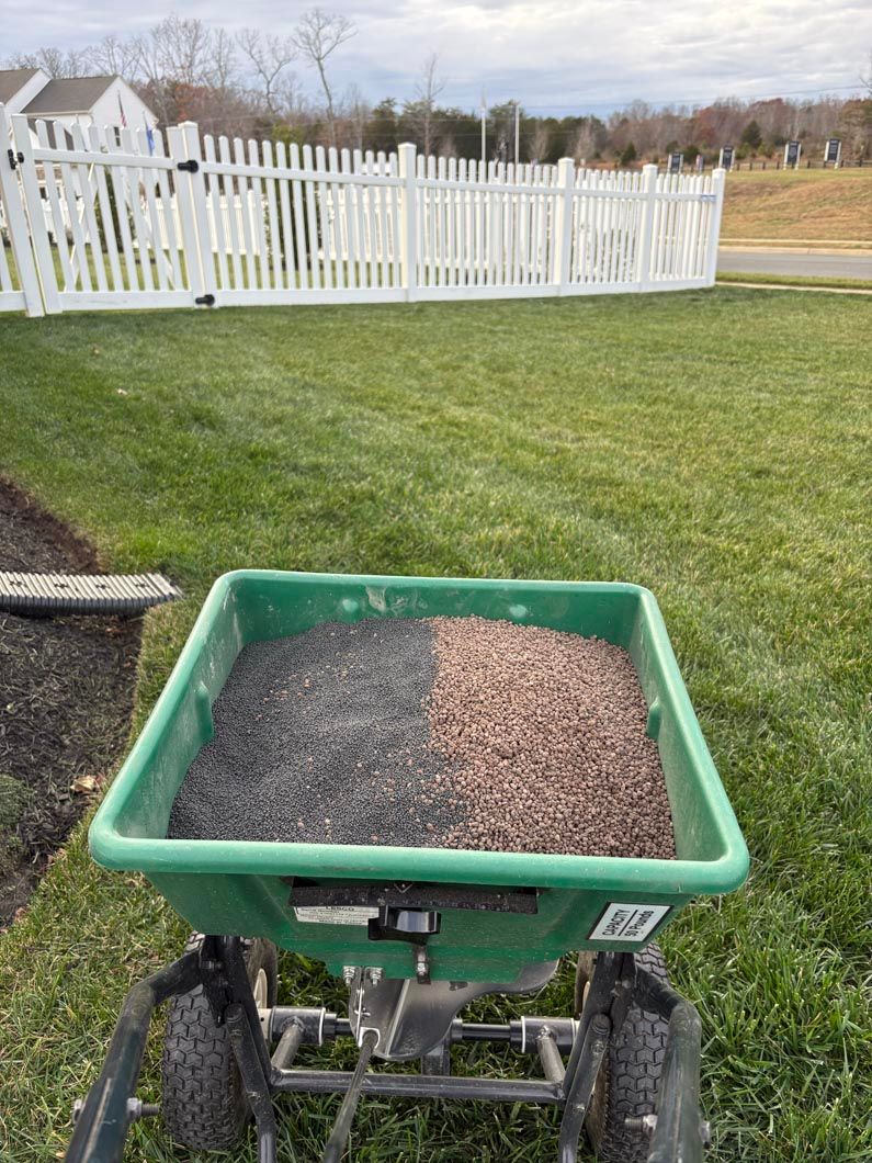 Green wheelbarrow filled with gravel on a lawn beside a white picket fence